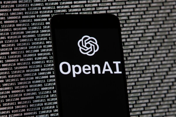The OpenAI logo appears on a mobile phone in front of a computer screen with random binary data, March 9, 2023, in Boston. (AP Photo/Michael Dwyer, File)